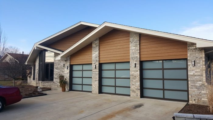 A modern home with three garage doors, each one comprised of a grid of dark grey glass